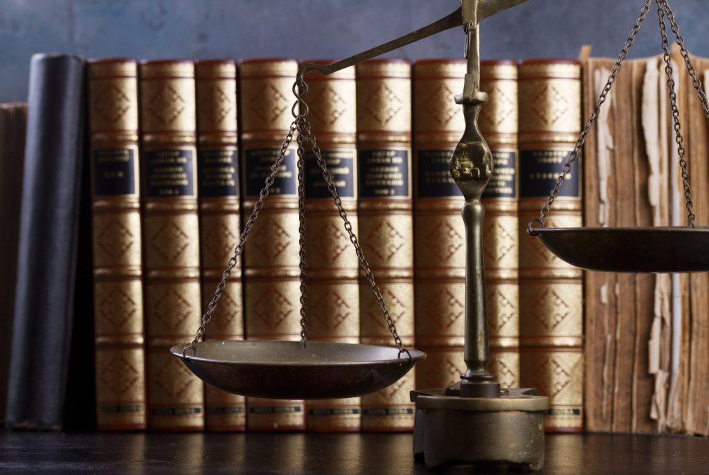 A brass balance scale in front of old leather-bound books, symbolizing law and justice. The scene evokes trust—essential for data destruction and electronics recycling for law firms with Omega ECycles.