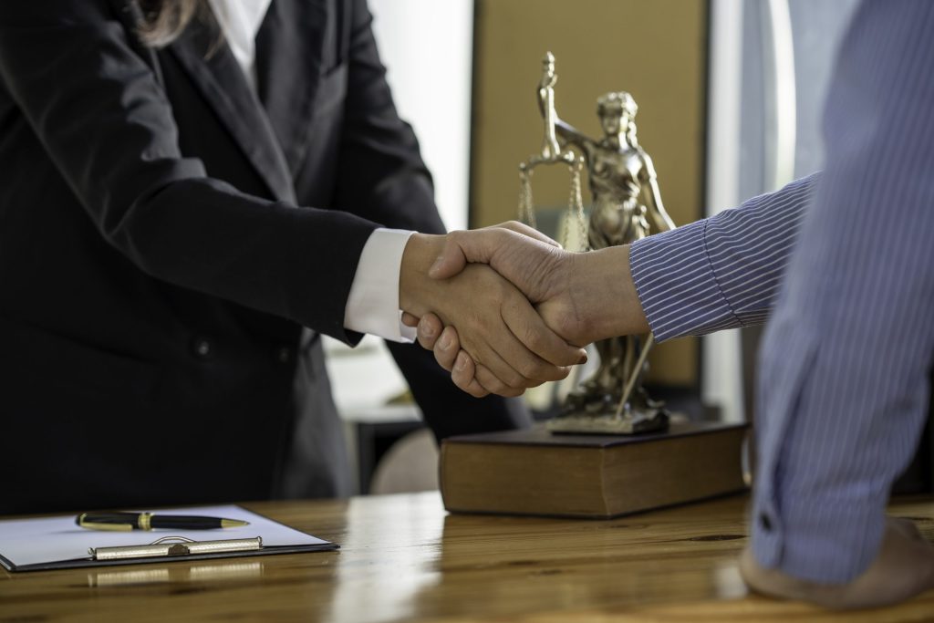 Two people in business attire shake hands across a desk with legal documents, a pen, and an Omega ECycles brochure, highlighting electronic pickup services for law firms along with secure data destruction in the background.