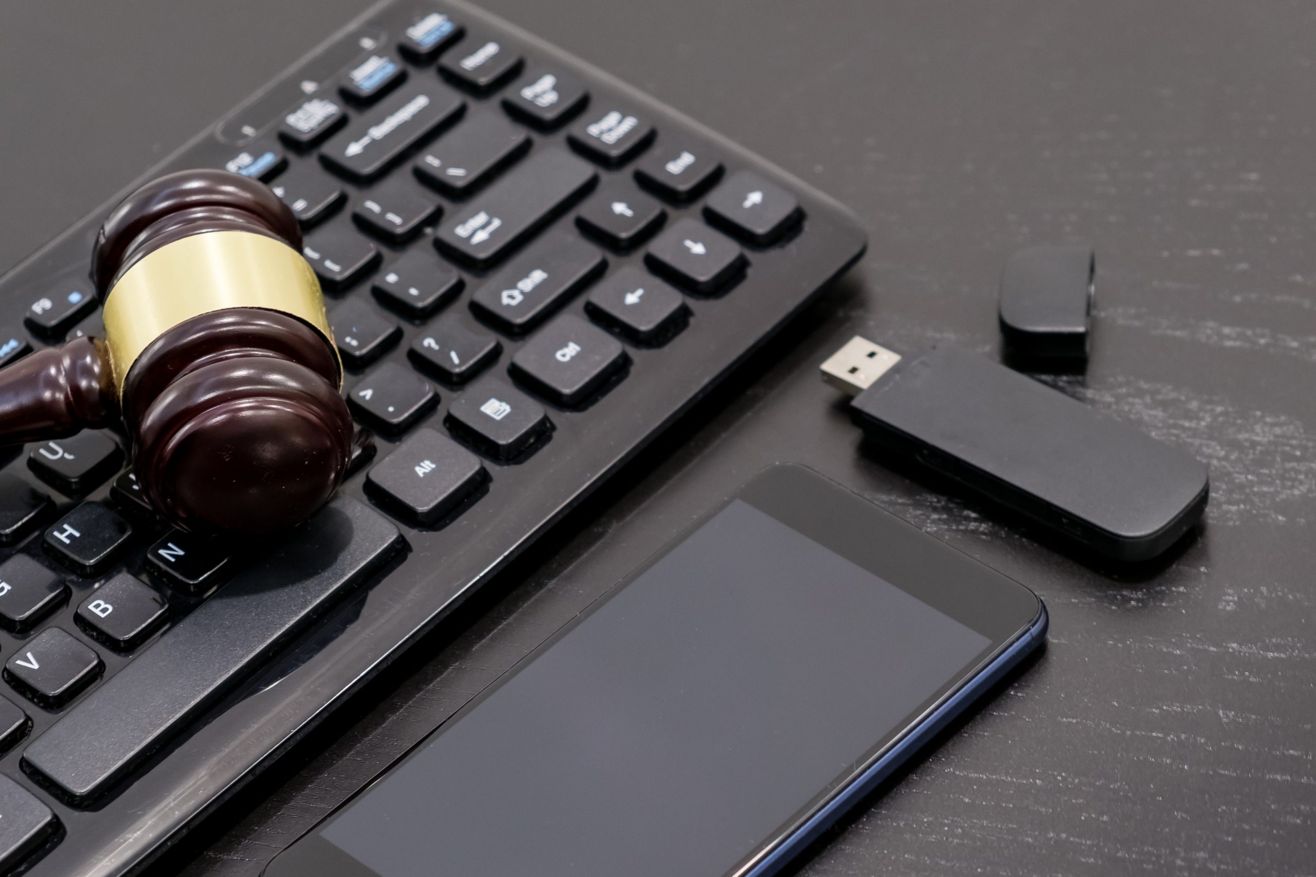 A judge’s gavel rests on a computer keyboard beside a smartphone and a USB flash drive on a dark desk, symbolizing digital justice and highlighting the importance of electronics recycling in law and technology.