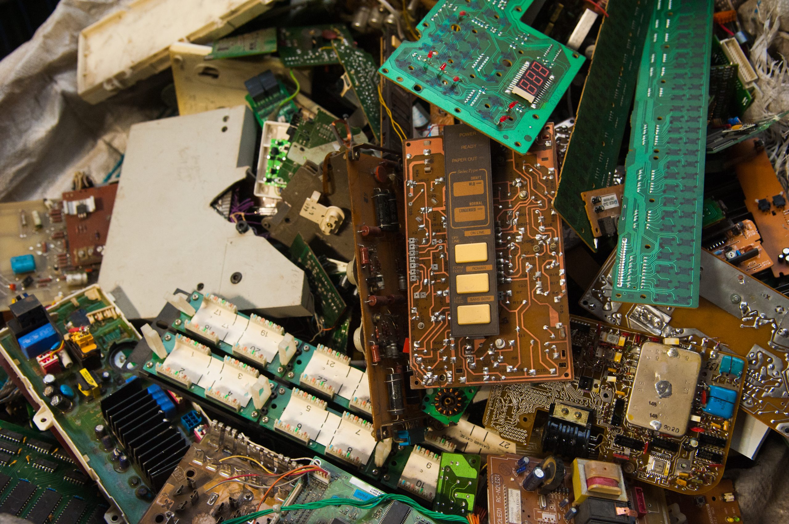 A pile of assorted electronic circuit boards and components, showing various colors, chips, and traces, stacked together in a chaotic arrangement of e-waste.