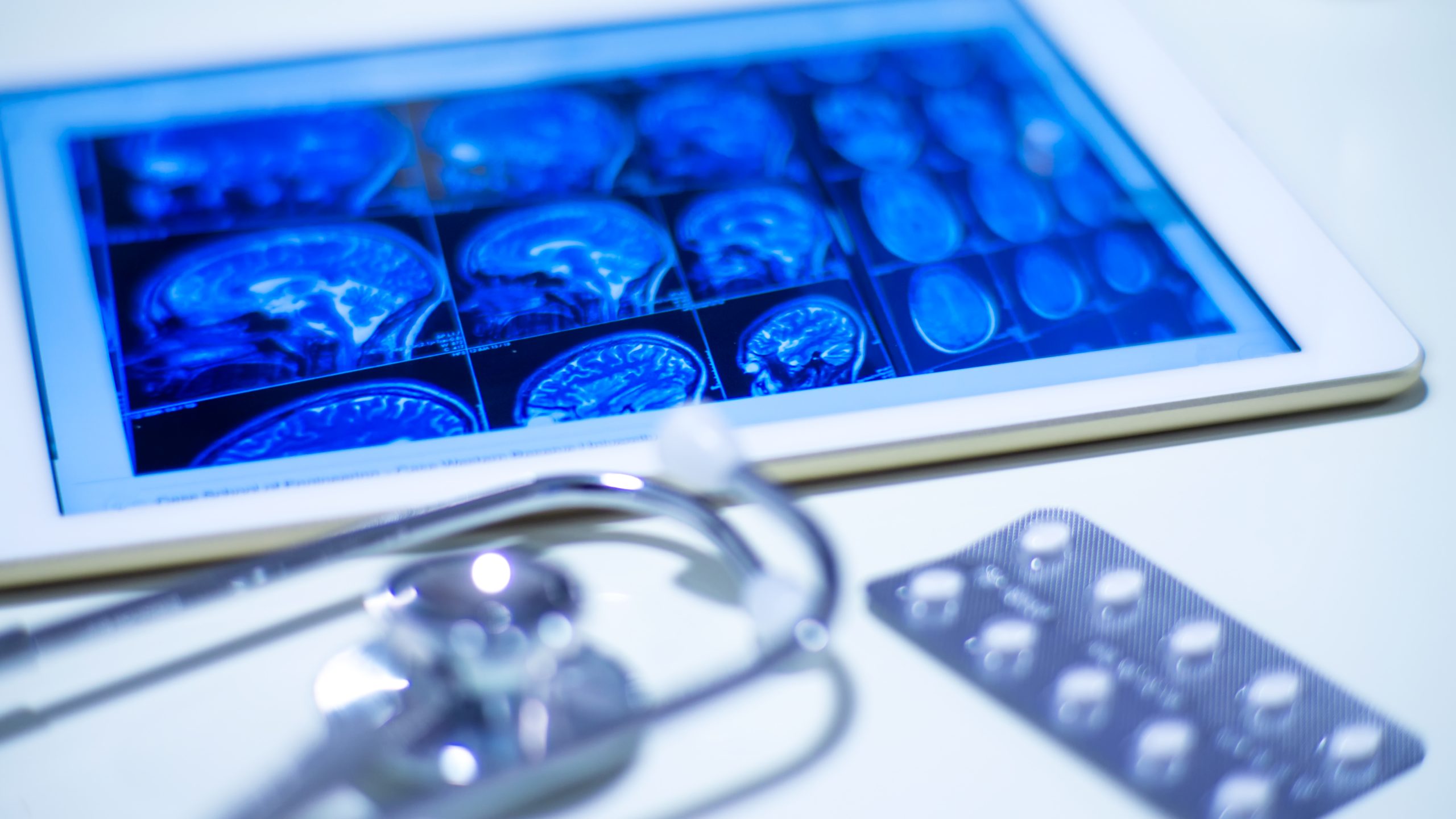 A tablet showing brain scan images rests on a white surface beside a stethoscope and pills, suggesting a neurology-focused healthcare setting where secure, free data destruction for healthcare is essential.