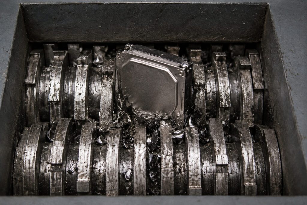 A metal hard drive undergoes hard drive shredding inside an industrial shredder, where multiple rotating blades break the device into pieces.