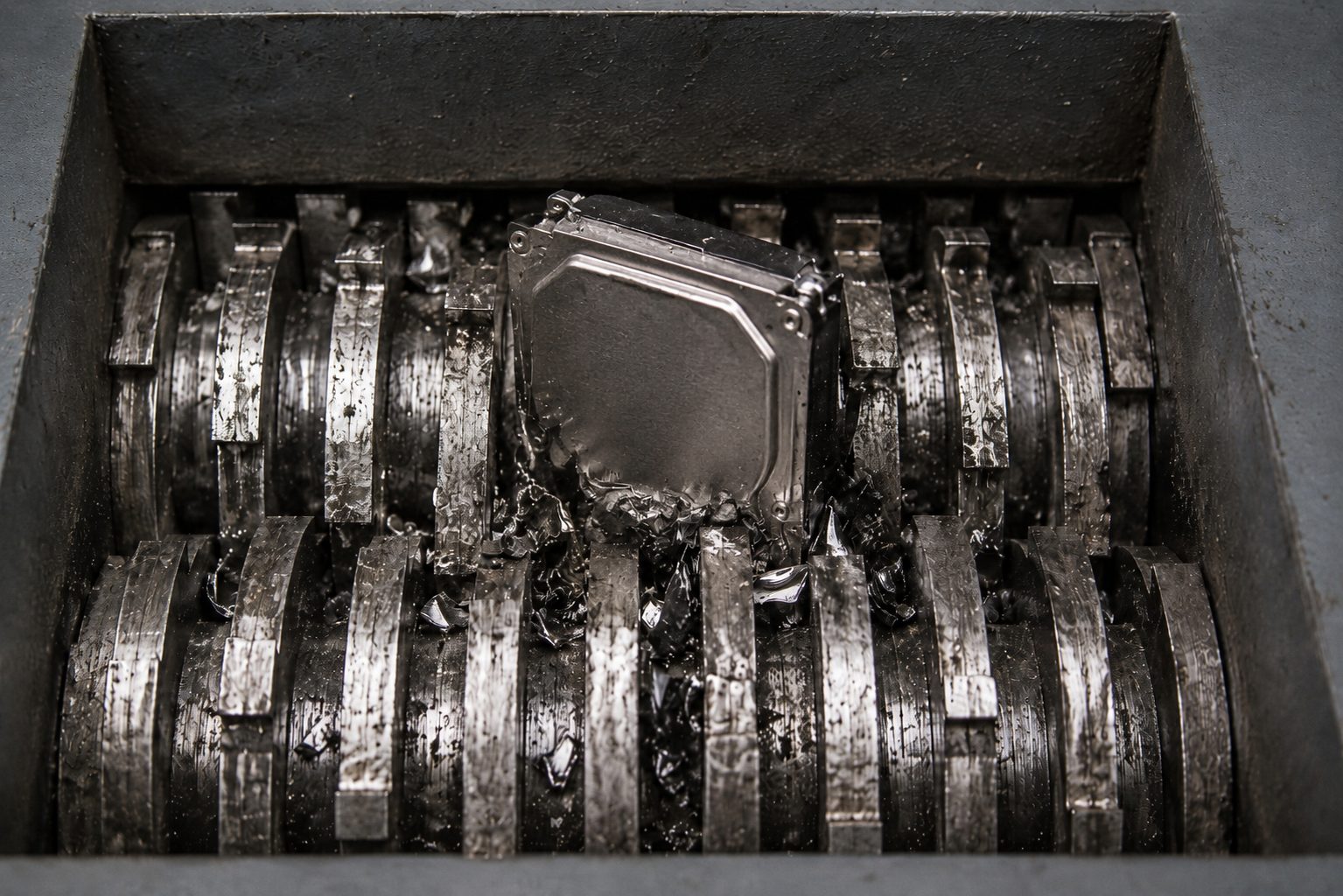A metal hard drive undergoes hard drive shredding inside an industrial shredder, where multiple rotating blades break the device into pieces.