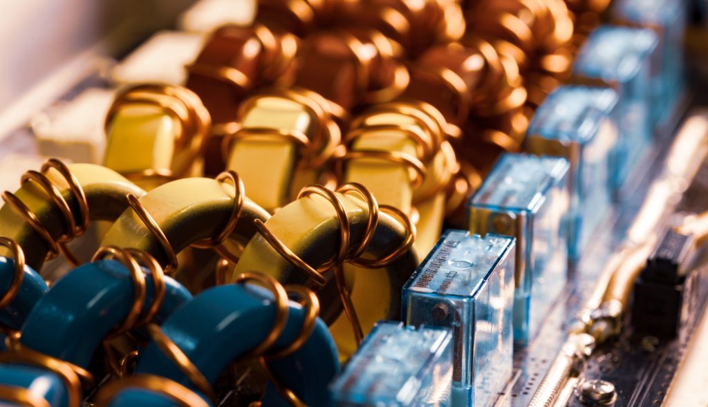 Close-up of colorful capacitors and copper coils on a circuit board, highlighting intricate electronic components—essential for electronics recycling—and featuring rows of blue, yellow, and brown elements with transparent blue connectors.