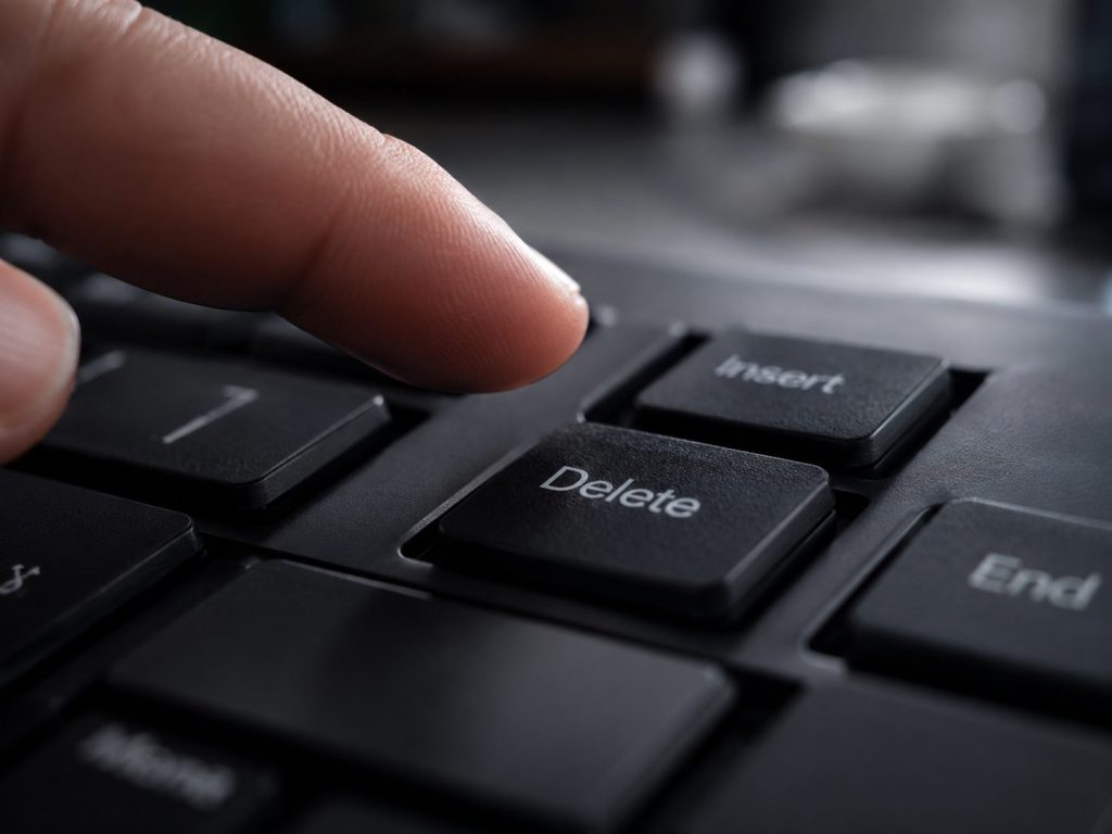 A close-up of a finger about to press the "Delete" key on a black computer keyboard, symbolizing the start of secure data removal—an essential step before utilizing a professional hard drive destruction service.
